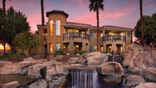 Ein Resort mit Wasserfall, mehreren Balkonen und einem Sonnenuntergangshimmel.