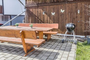 Un espace extérieur aménagé en bois, avec un banc et des tables, un barbecue et une clôture en bois décorée de motifs de papillons.