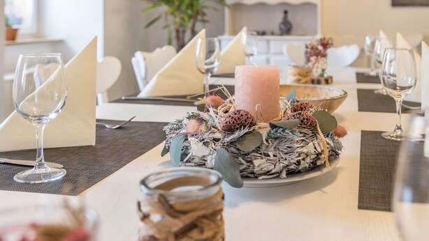 Una mesa de comedor preparada con cristalería, servilletas y un centro de mesa con una vela y elementos decorativos.