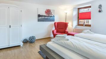 A bedroom with a bed, a red chair, a white wardrobe, a lamp, and a window with a red blind.