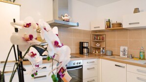 Een moderne keuken met witte kastjes, een ingebouwde oven, een koffiezetapparaat en een plank met keukengerei.