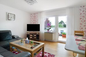 Una sala de estar con sofá, mesa de centro, televisor y vista al exterior.
