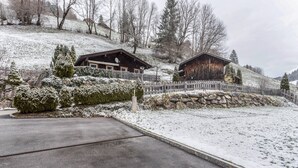 A snow-covered landscape with two wooden cabins, a stone wall, and a metal fence.