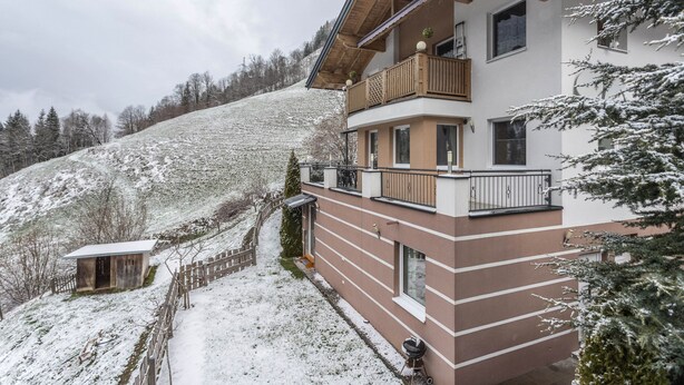 A multi-story building with balconies, a wooden fence, and a snow-covered hill in the background.