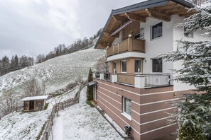 A multi-story building with balconies, a wooden fence, and a snow-covered hill in the background.