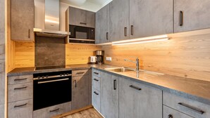 A modern kitchen with grey cabinets, a built-in oven, a microwave, and a coffee maker.