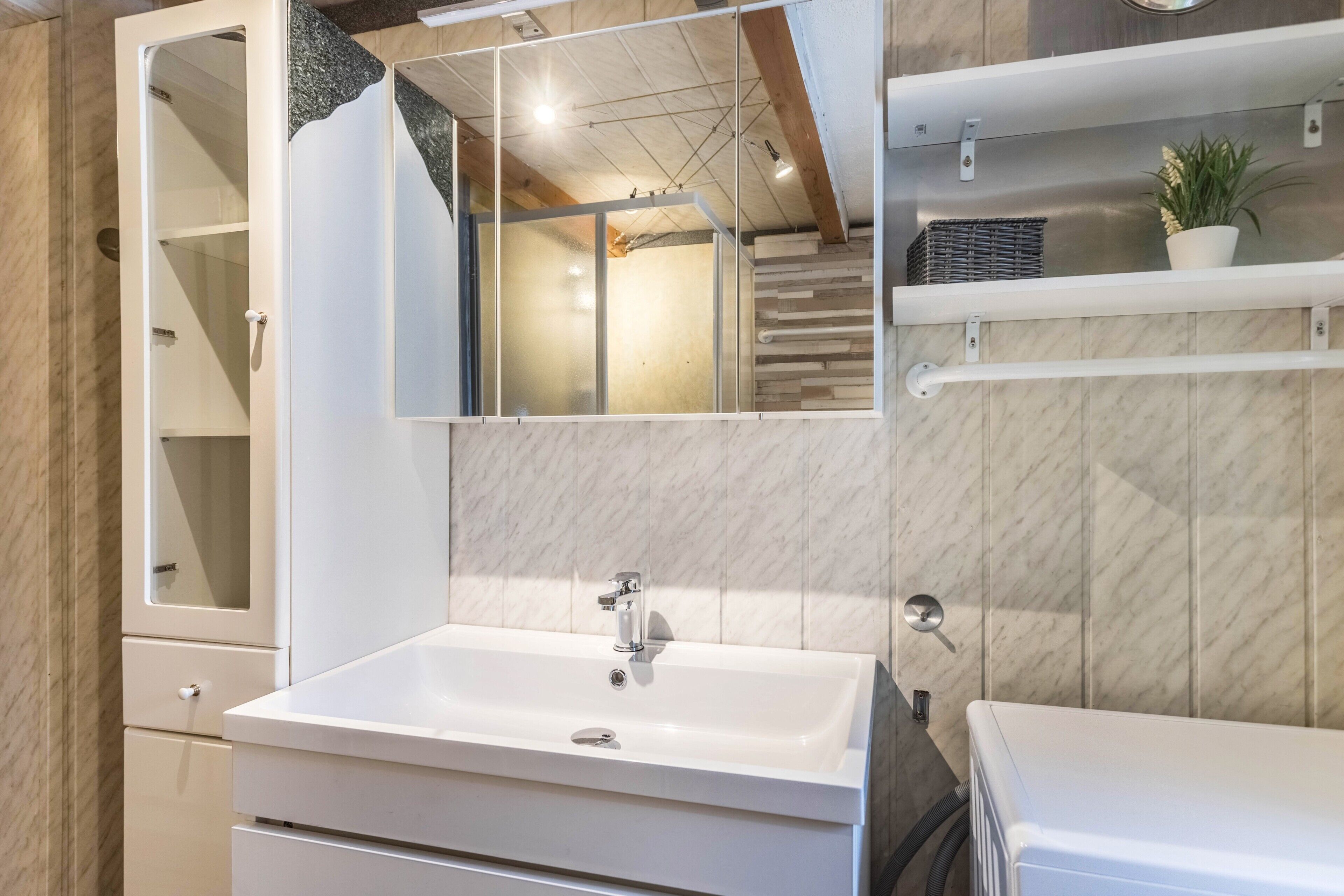 Een badkamer met een wit wastafel, een spiegel en een douchehoek.