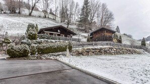 Un paisaje nevado con dos cabañas de madera, un muro de piedra y una valla de madera.