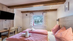 Un dormitorio con dos camas, televisión, ventana con cortinas y vigas de madera en el techo.