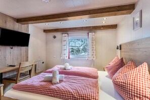 Une chambre avec deux lits, une télévision, une fenêtre avec des rideaux et des poutres en bois au plafond.