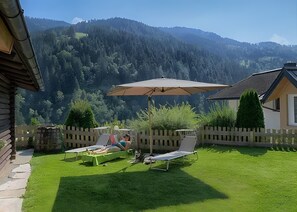 A backyard with two lounge chairs, a large umbrella, and a wooden fence. - Holiday flat 'Chalet Berger' with mountain view, communal garden and WiFi. (St. Johann im Pongau)