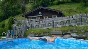 Un hombre descansando en una piscina con un muelle de madera y una cabaña al fondo.