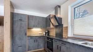 Una cocina moderna con armarios grises, horno empotrado y ventana con persianas.