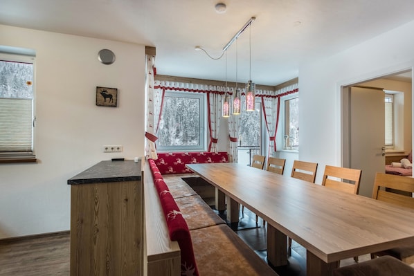 A dining area with a long wooden table, benches, and a window with curtains.