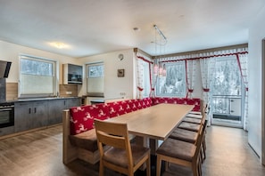A kitchen with a dining area, including a wooden table and benches, a built-in oven, and a window with curtains.