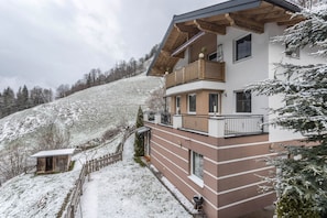 Ein mehrstöckiges Gebäude mit Balkonen, einem Holzzaun und einem schneebedeckten Hügel im Hintergrund.