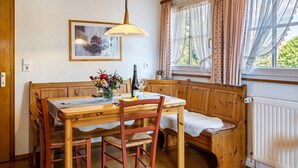 Een houten eettafel met banken, een kroonluchter, een raam met gordijnen en een radiator.