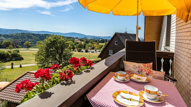 Een balkon met een gedekte tafel voor thee, een gele parasol en een mooi uitzicht op een huis en het landschap.