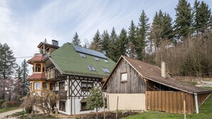 Una casa tradicional de entramado de madera con techo inclinado, paneles solares y un granero de madera.
