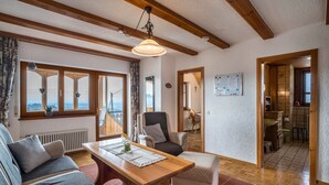 Una sala de estar acogedora con una mesa de madera, sofá y sillón, ventanas amplias y vistas al exterior.