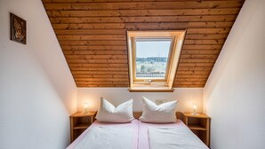 Un dormitorio con techo inclinado, tragaluces, dos mesitas de noche con lámparas y una cama con almohadas.