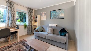 Una sala de estar moderna con un sofá gris, una mesa de centro de madera, una estantería y un ventanal con cortinas.