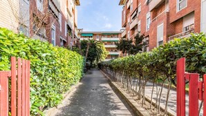 Un estrecho callejón entre edificios con un sendero pavimentado, rodeado de follaje y portones rojos.