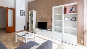 Una sala de estar moderna con un televisor de pantalla plana, estanterías blancas, una mesa de centro y un sofá.