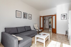 Un salon moderne avec un canapé gris, une table basse blanche et des œuvres d’art encadrées accrochées au mur.
