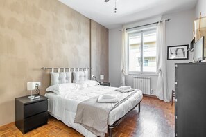 A bedroom with a bed, a nightstand, a dresser, a window with curtains, and a radiator. - GuestHost - Modern apartment of 80 square meters, which can accommodate up to 4 people, located on the fourth floor of a building with a lift (steps to access). The property is located a few meters from Lungarno and Cascine Park, in an area ideal for wal (Firenze)