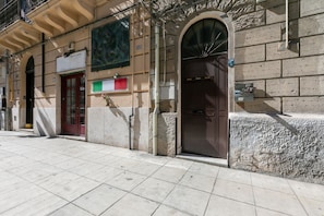 A building facade with a red door, a green and white sign, and a stone wall.