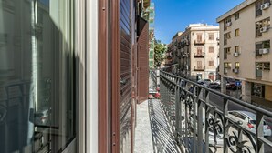 Ein schmaler Balkon mit Metallgeländer, der auf eine Straße mit parkenden Autos und Gebäuden blickt.