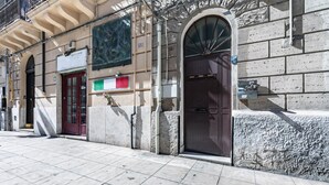 A building facade with a large arched entrance, a red door, and a sign above the door.