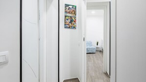 A hallway with a door leading to a room with a bed and a window.
