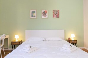 Un lit bien fait, avec du linge de lit blanc, deux lampes de chevet et trois œuvres d’art encadrées accrochées au mur.