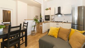 A modern kitchen with white cabinets, a stainless steel refrigerator, and a dining area with a wooden table and chairs. - GuestHost - Borgo Po Comfortable Apartment x4 (Torino)