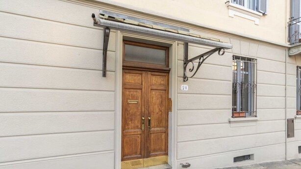 A building with a wooden double door, a small window with a metal grill, and a number '28' on the wall. - GuestHost - Borgo Po Comfortable Apartment x4 (Torino)