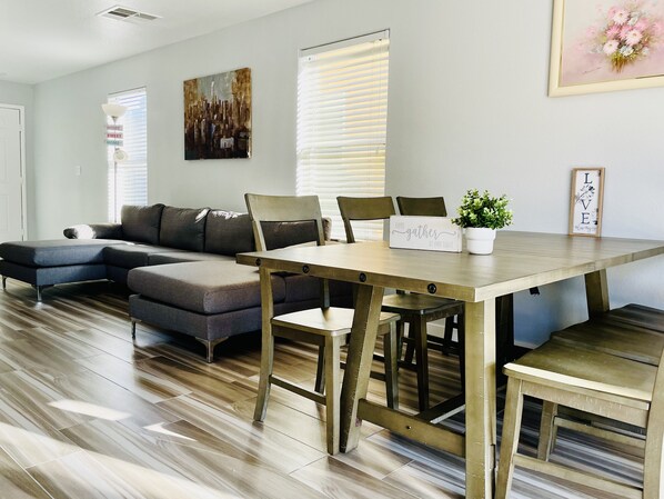 A modern living room with a sectional sofa, a wooden dining table, and a potted plant.