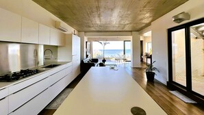 A modern kitchen with a central island, a dining area with a view, and a large sliding glass door leading to a balcony. - Air-conditioned villa for 7 people with sea view, rooftop, and beach access in Hyères (HYERES)