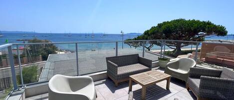 A balcony with wicker furniture, a view of the sea, and a tree.