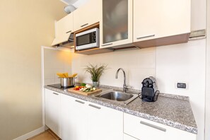 Una cocina moderna con armarios blancos, un lavamanos de acero inoxidable, un microondas y una máquina de café.