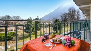 Un balcó amb una taula preparada per esmorzar, que inclou croissants, raïm i una poma verda, amb vista a un parc i una muntanya.