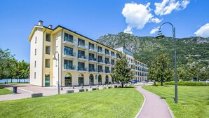 Un hotel de diverses plantes amb façana groga, un camí pavimentat i un paisatge de muntanyes al fons.