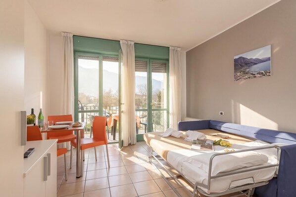 A hotel room with a bed, a sofa, a dining table with chairs, and a view of the outdoors.