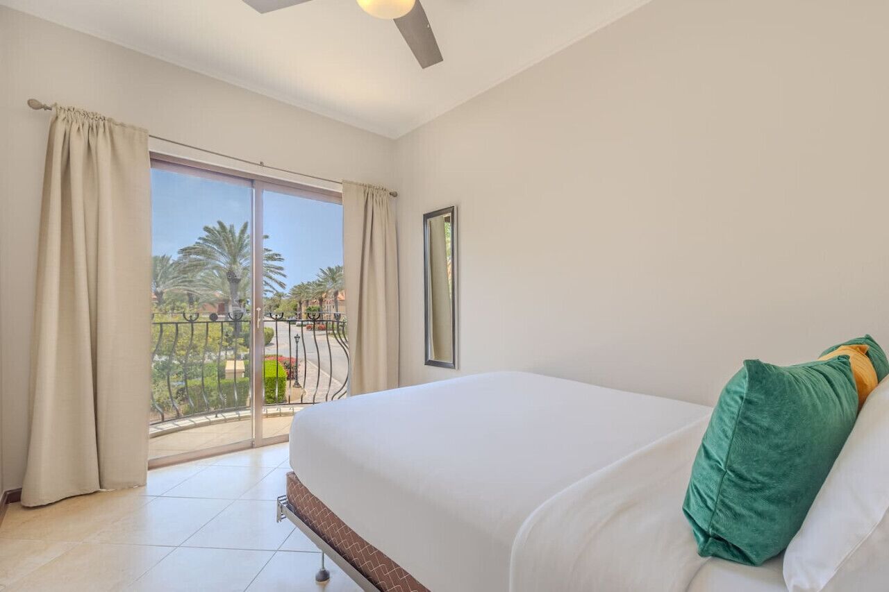 Ein Hotelzimmer mit einem großen Bett, einem Balkon mit Blick auf Palmen und einem Deckenventilator.