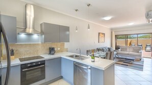 A modern kitchen with a built-in oven, dishwasher, and a large island with a sink. There is a dining area with a sofa and a coffee table. - LUX 2BR Condo | Gold Coast Pools & Gym Near Malmok (Noord)