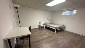 Een kamer met een bed, een bureau, een stoel, een lamp en een raam.