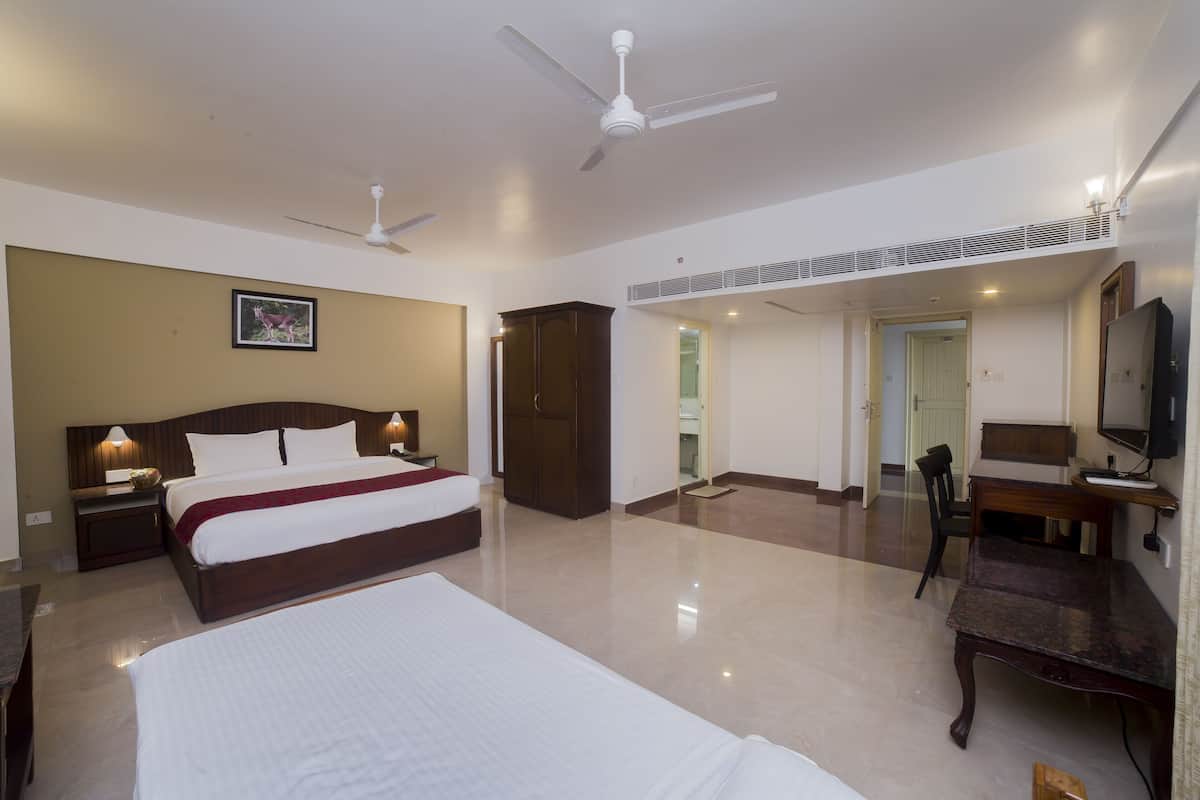 A hotel room with a large bed, two bedside tables, a desk, a chair, a ceiling fan, and a TV.