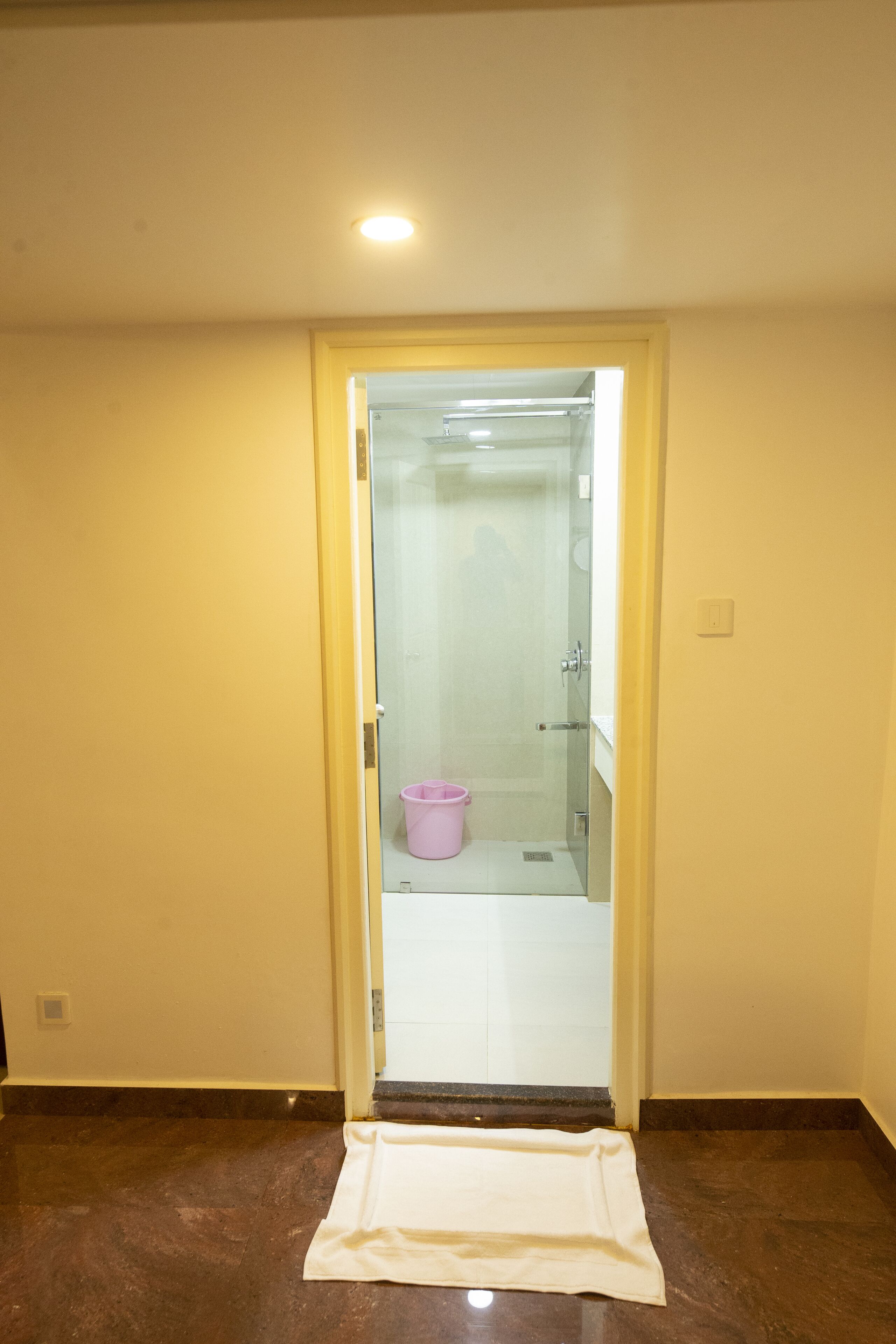 A bathroom with a glass door, a white towel on the floor, and a pink bucket.