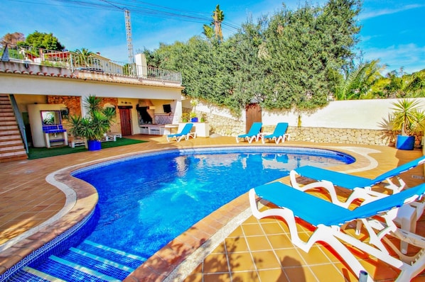A swimming pool with blue tiles, surrounded by lounge chairs and potted plants.